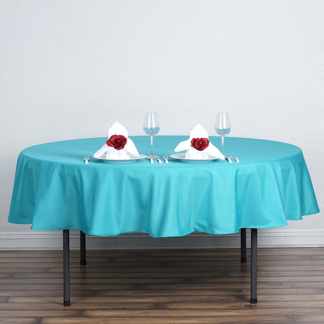 Turquoise tablecloth with elegant red rose napkins on a round table setting.