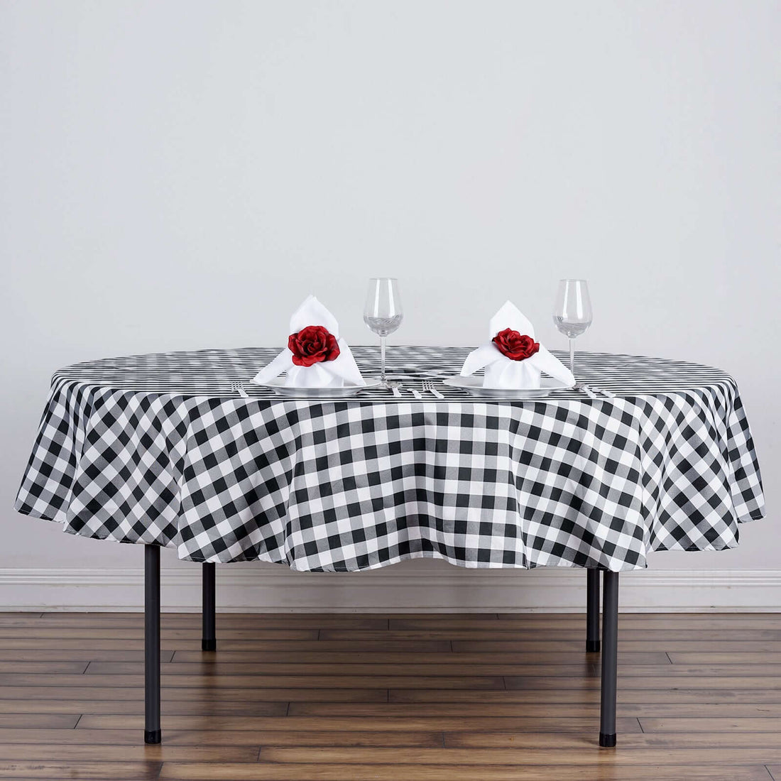 Round table set with black and white checkered tablecloth, decorated with flowers and glasses.