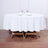 Round white tablecloth draped over a wooden table with plates and glasses