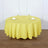 Round yellow tablecloth on a dining table with glassware and napkins.