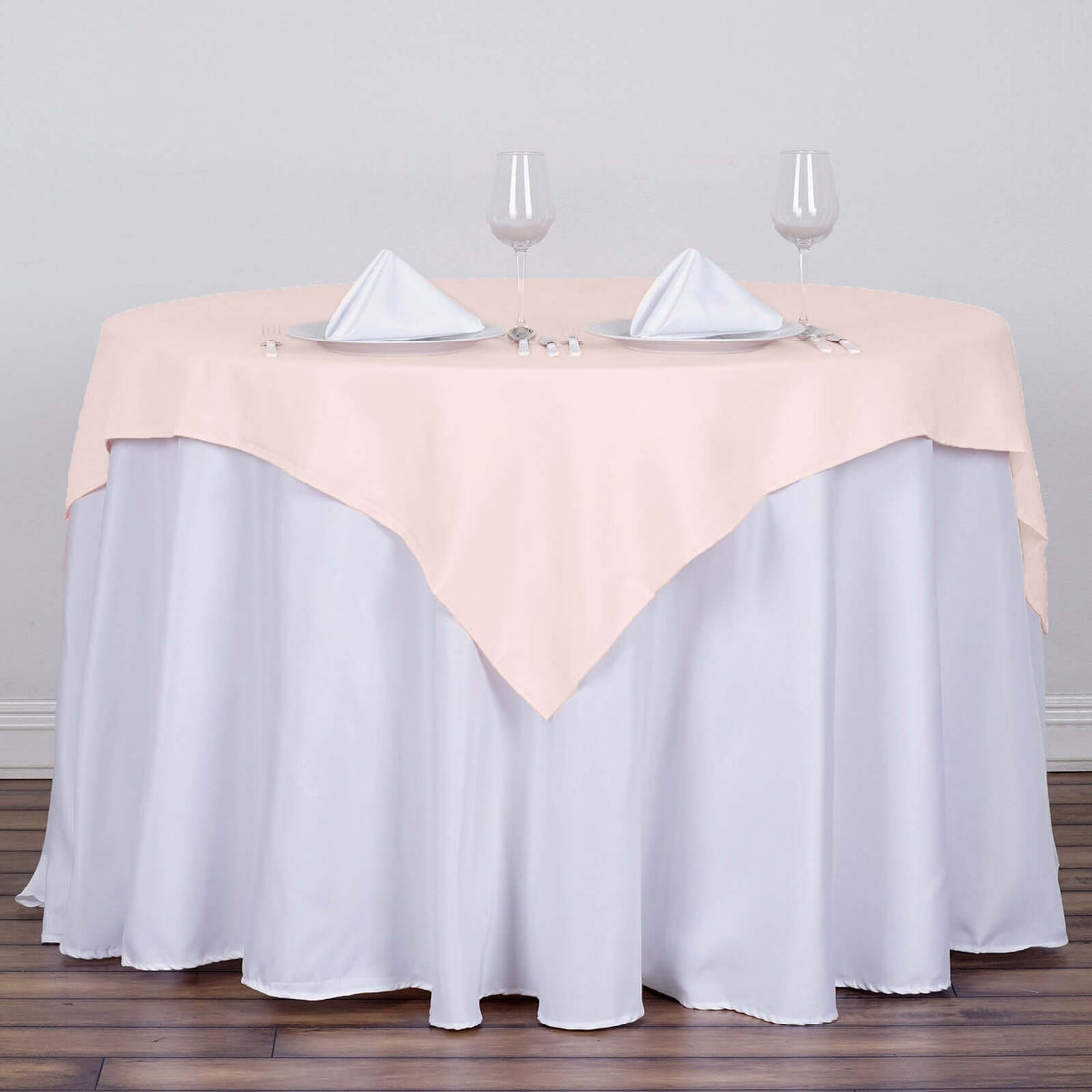 Peach tablecloth draped over a round table set with glasses and napkins.