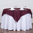 Elegant burgundy tablecloth draped over a white table with plates and glasses.