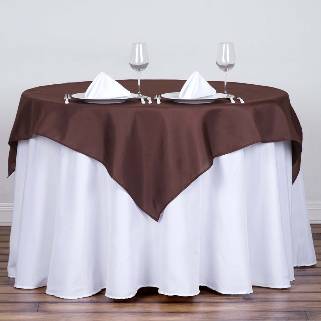 Brown tablecloth draped over a round table set for two with glasses and napkins.