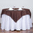 Brown tablecloth draped over a round table set for two with glasses and napkins.
