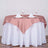 Rose tablecloth draped elegantly over a round table with glassware and napkins.