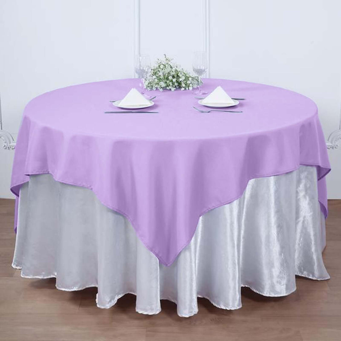 Round lavender tablecloth on a silver table skirt in a staged dining setting.