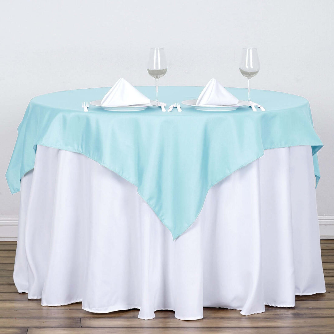 Round table set with aqua blue and white tablecloth, glasses, and napkins.