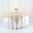 Beige tablecloth draped over a round table with white undercloth and floral centerpiece.
