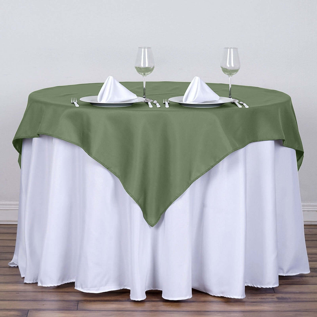 Green tablecloth draped over a white table with dinnerware and glassware.