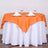Round table set with orange tablecloth and white napkins in a dining setup.