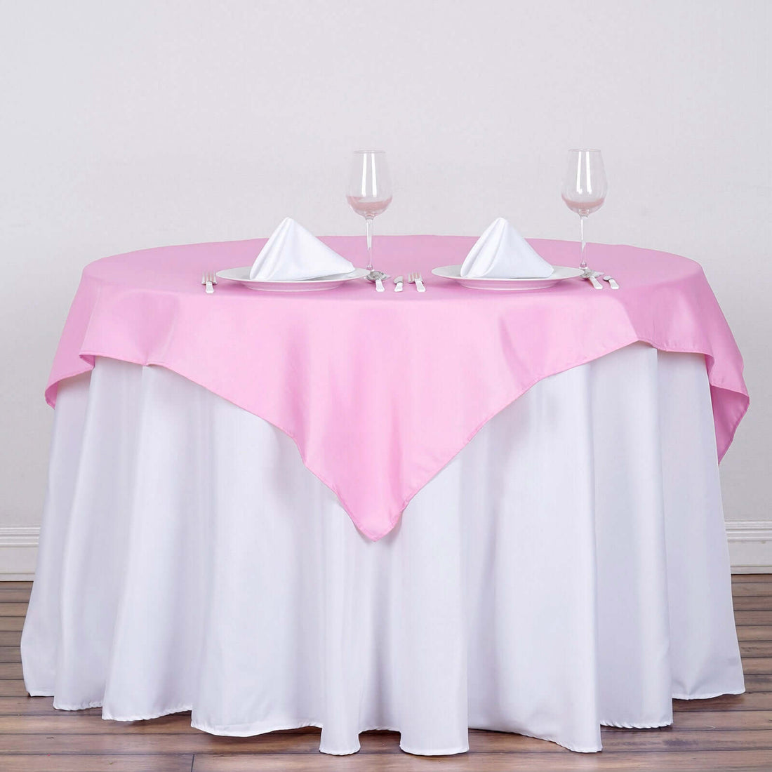 Pink tablecloth draped over a round table set for two with glasses and napkins.