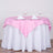 Pink tablecloth draped over a round table set for two with glasses and napkins.