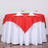 Red tablecloth draped over a round white table set for dining.