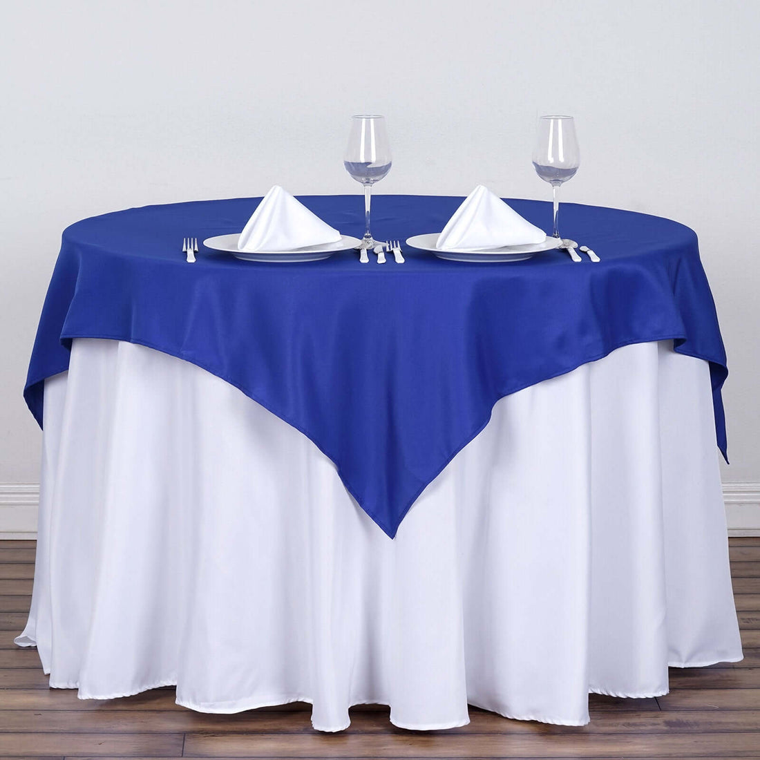 Blue tablecloth draped over a round table set with glasses and napkins.