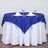 Blue tablecloth draped over a round table set with glasses and napkins.