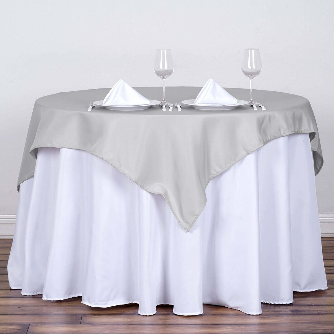 Round table set with a gray and white tablecloth, two napkins, and two wine glasses.