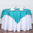 Teal satin tablecloth on a round table with dinnerware and glasses.