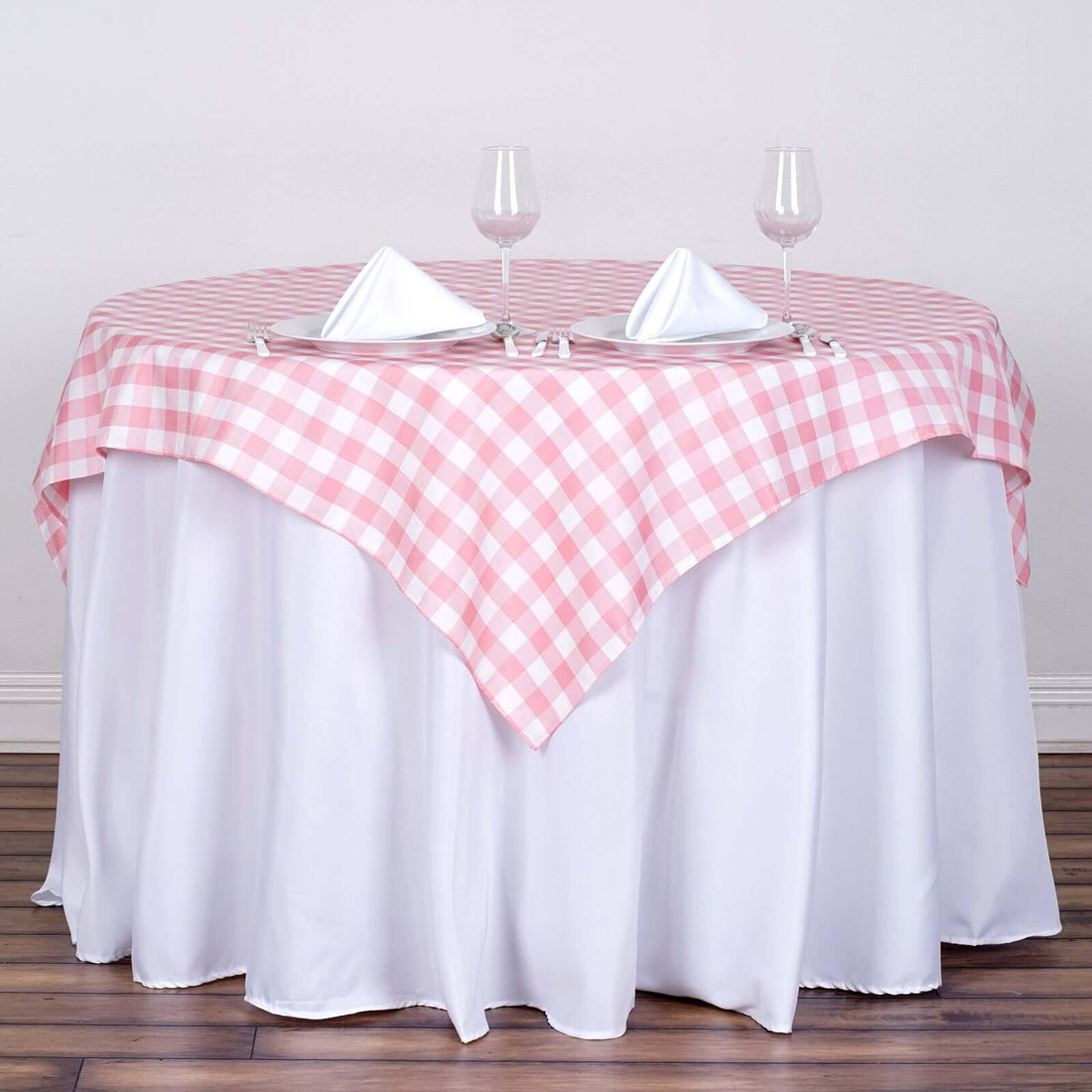 Pink gingham tablecloth draped over a round white table with glasses and napkins.