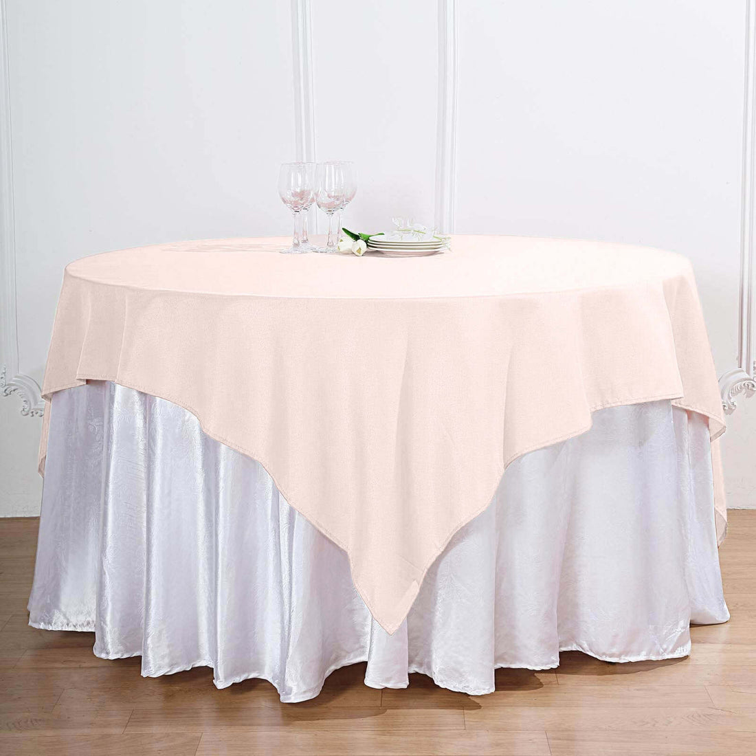 Round tablecloth in soft pink draped over a white satin table.