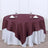 Round burgundy tablecloth draped over a white table with glassware and napkins.