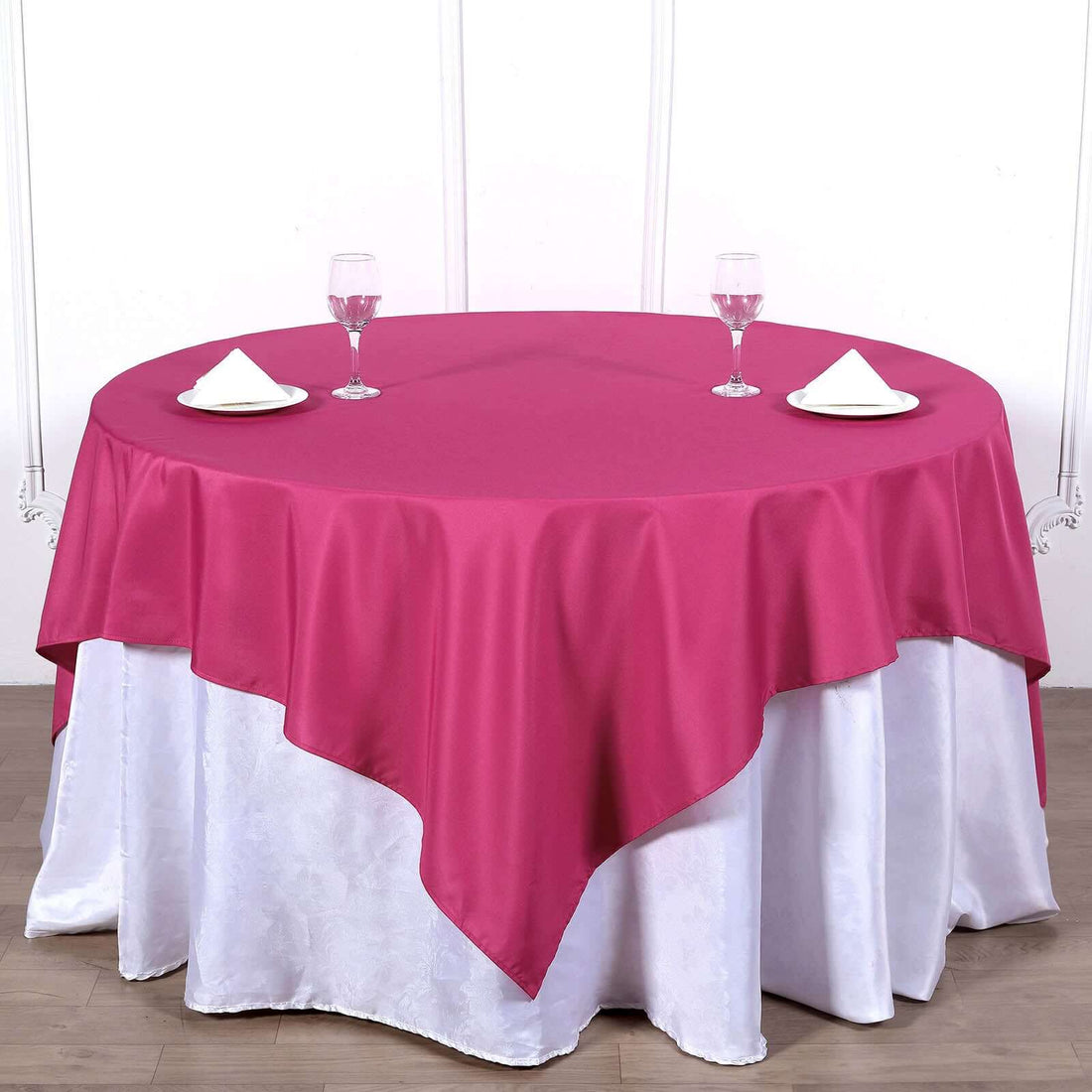 Round maroon tablecloth draped elegantly over a white table setting with glasses and napkins.