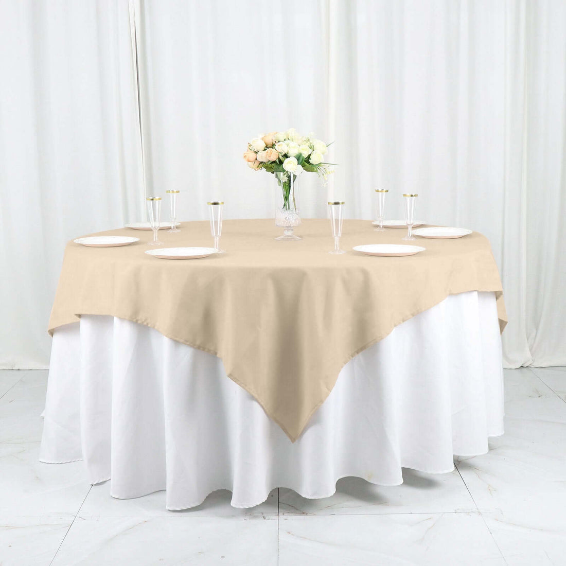 Beige round tablecloth draped elegantly over a white table with floral centerpiece.