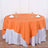 Round orange tablecloth draped over a table with glasses and napkins.