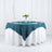 Elegant teal tablecloth draped over a round table set with plates and candles.