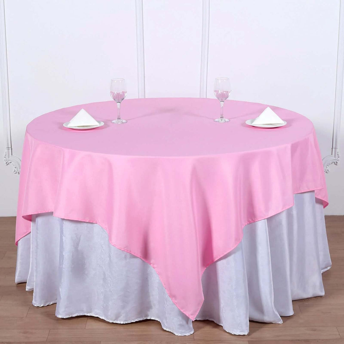 Round table set with pink and silver tablecloths, glasses, and napkins.