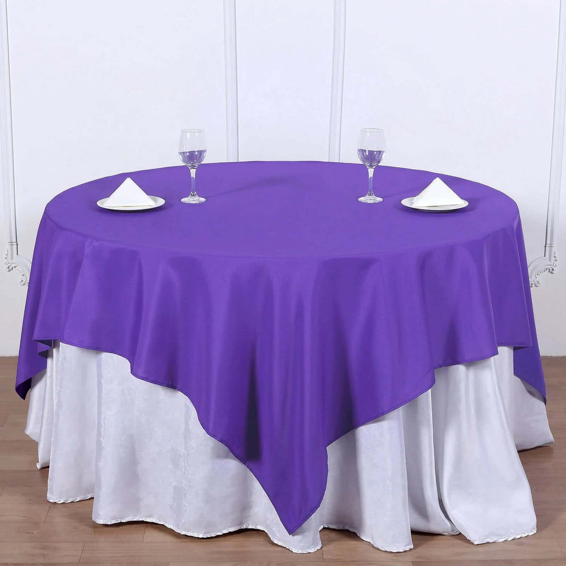 Purple round tablecloth with napkins and glasses on a white table.