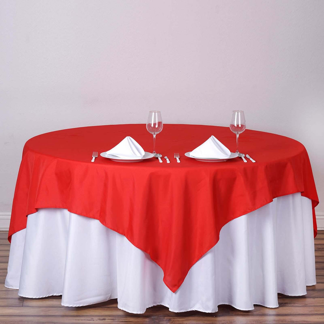 Red tablecloth draped over a round table set for dining with glasses and napkins.