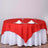 Red tablecloth draped over a round table set for dining with glasses and napkins.