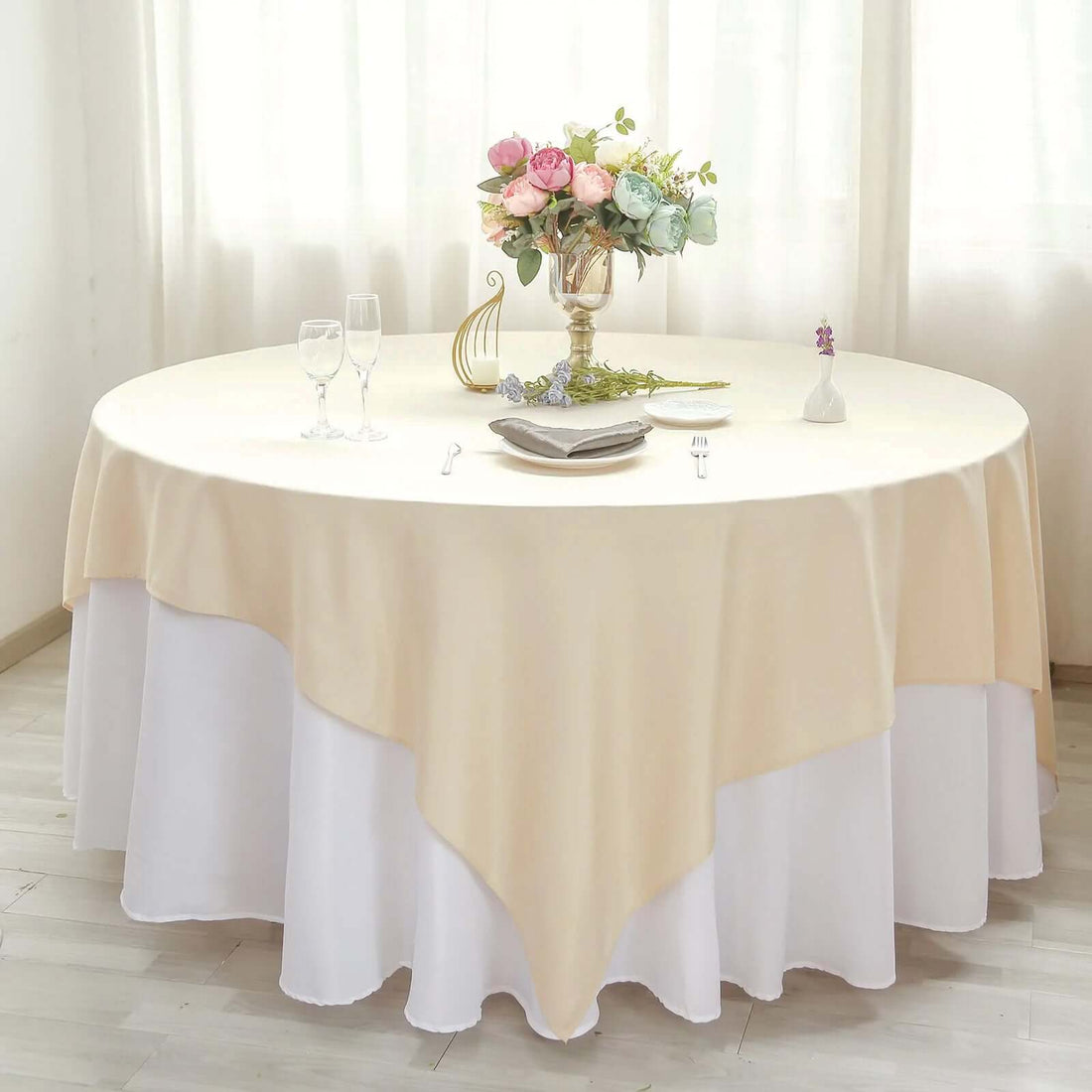 Round table set with an elegant beige and white tablecloth, floral centerpiece, and glassware.