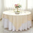 Round table set with an elegant beige and white tablecloth, floral centerpiece, and glassware.