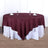 Burgundy round tablecloth on a white table with glasses and napkins