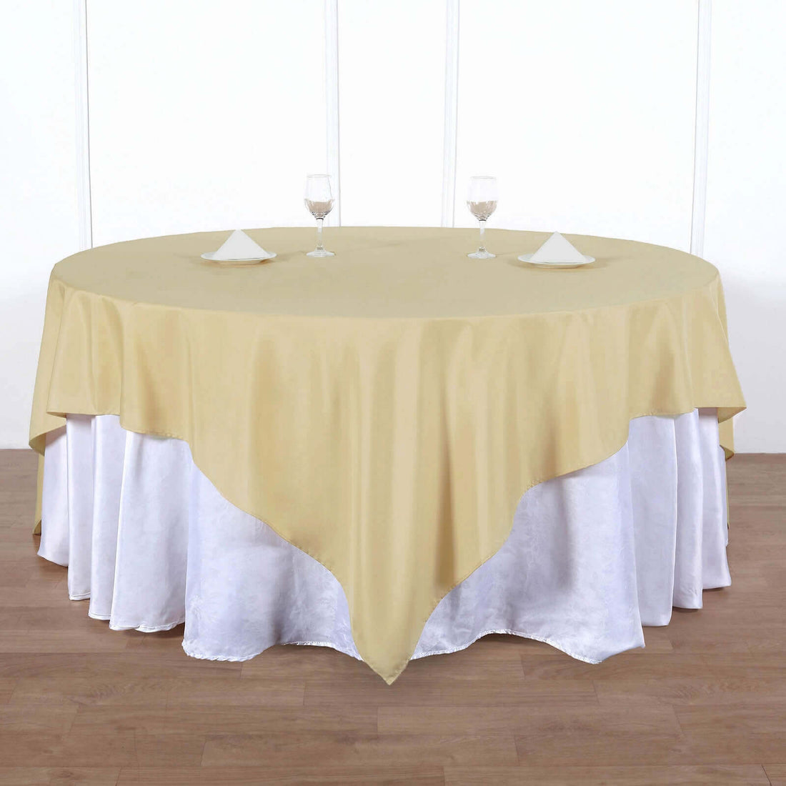 Round gold tablecloth draped over a white table with glasses and napkins.