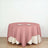 Round table with a pink and cream tablecloth, set with three plates.