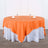 Round orange tablecloth on a white table with glasses and napkins.