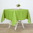 Green tablecloth draped over a wooden table with a flower arrangement on top.