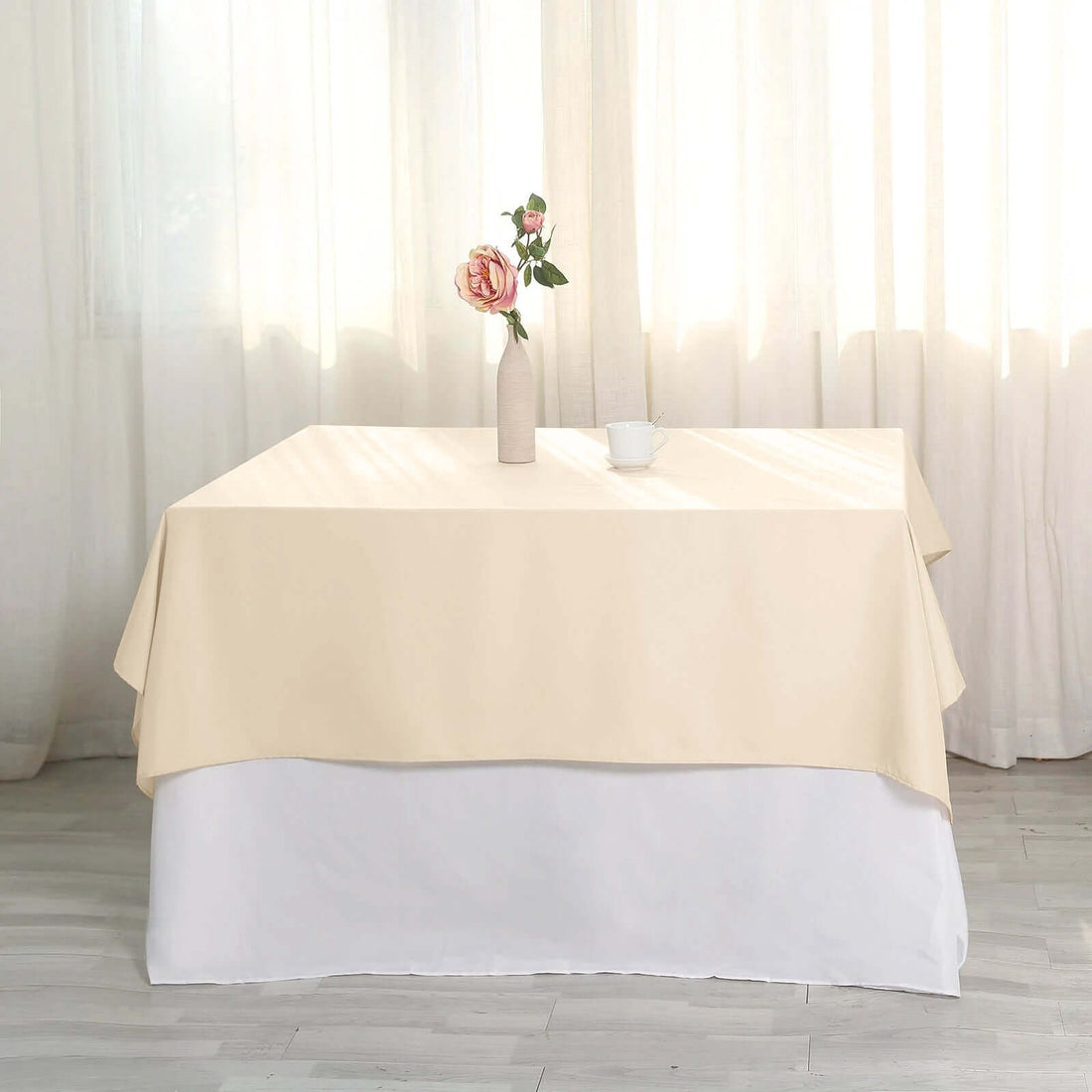 Beige tablecloth draped elegantly over a white table, styled with a vase and cup.