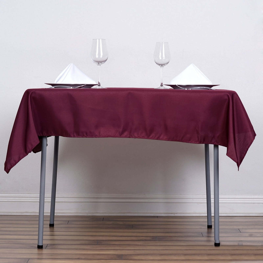 Table set with burgundy tablecloth, plates, and glasses for a dining experience.