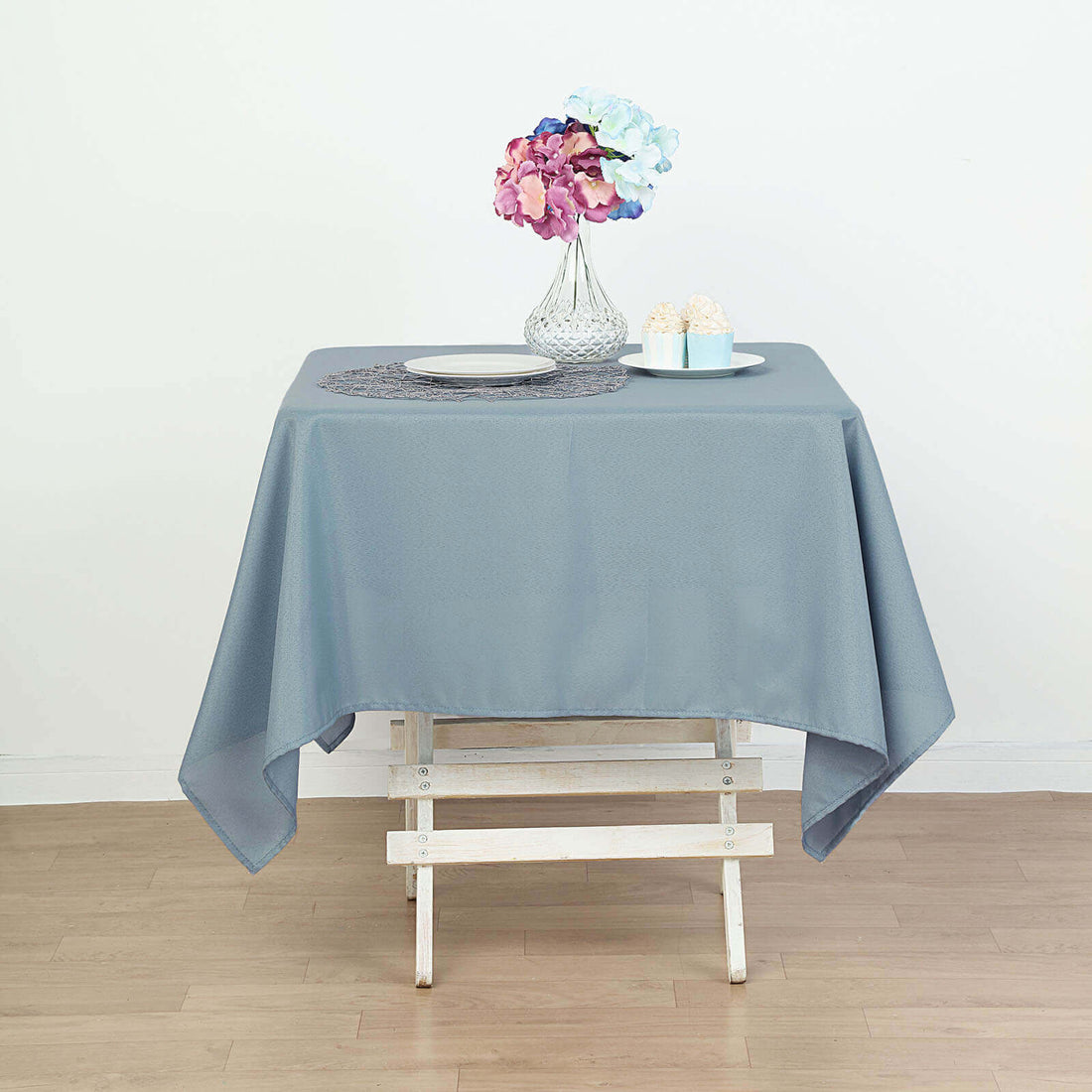 Gray tablecloth draped over a white wooden table with a flower vase and dessert plates.