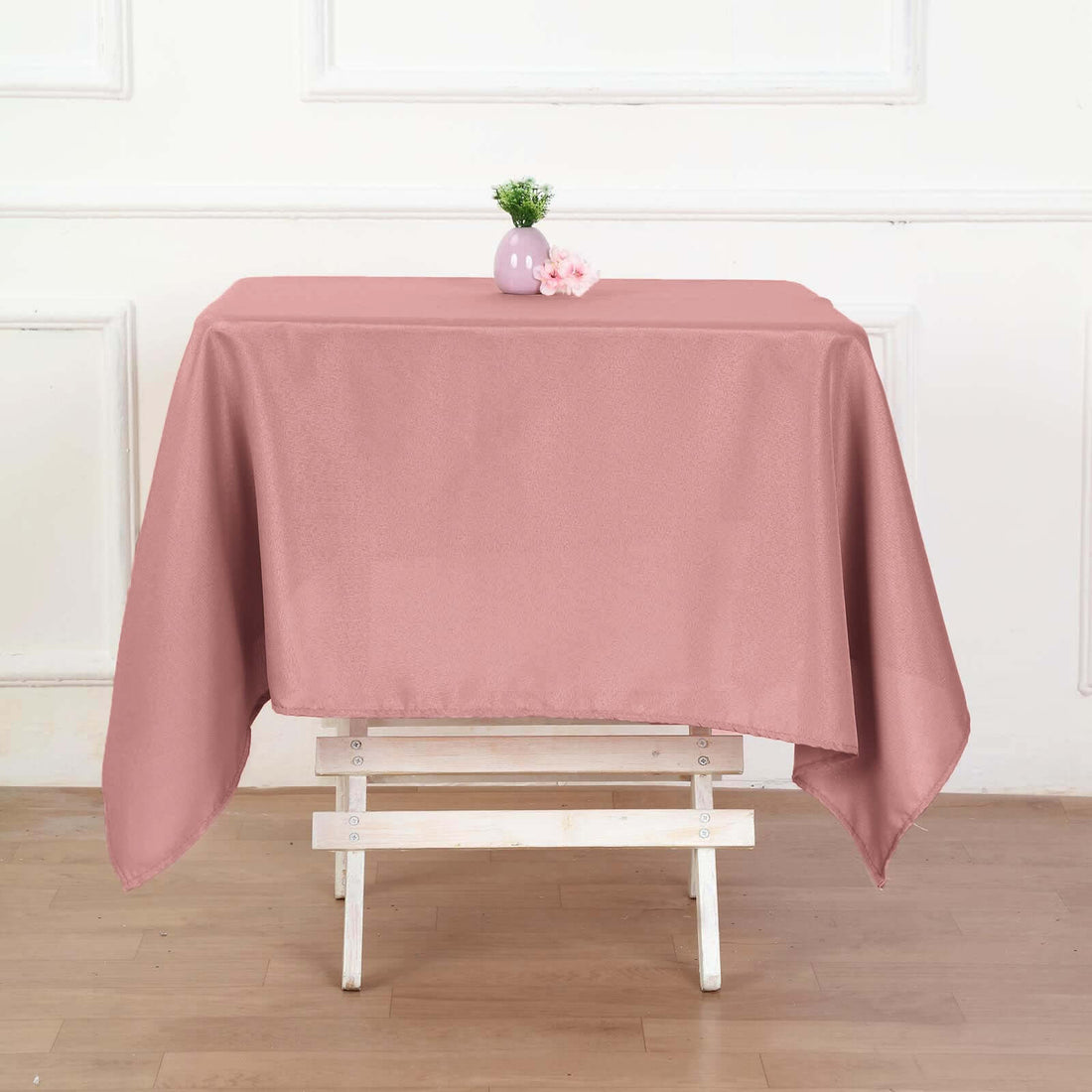 Pink tablecloth draped over a white wooden table with decorative vase and flowers.