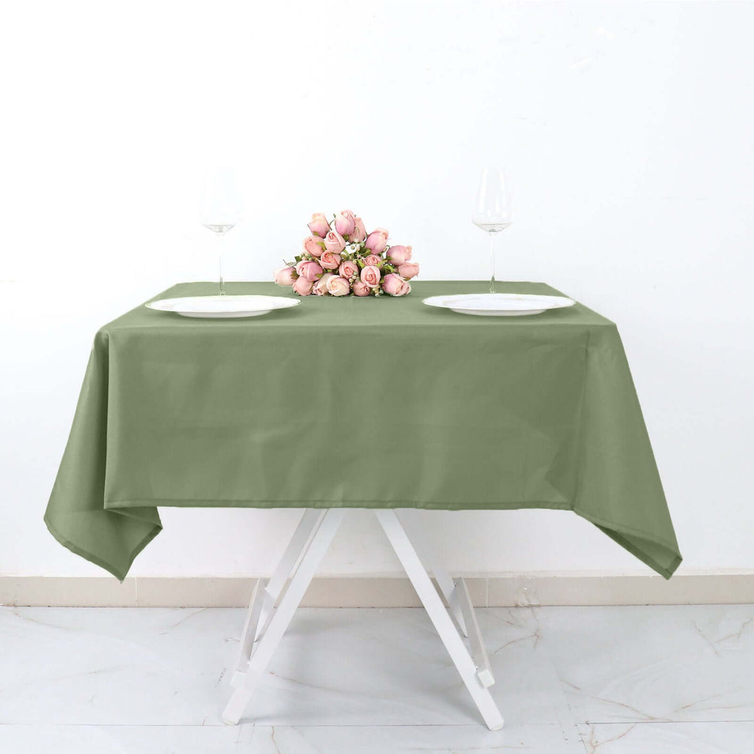 Green tablecloth with plates and floral centerpiece on a table.