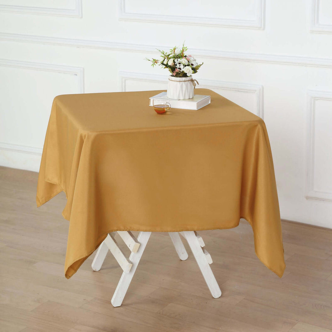 Gold tablecloth draped on a white table, styled with a vase and book.