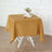 Gold tablecloth draped on a white table, styled with a vase and book.