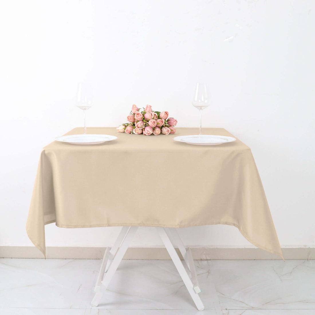 Beige tablecloth set with wine glasses and a flower arrangement on a white backdrop.