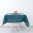 Teal tablecloth with plates and floral centerpiece on a dining table.