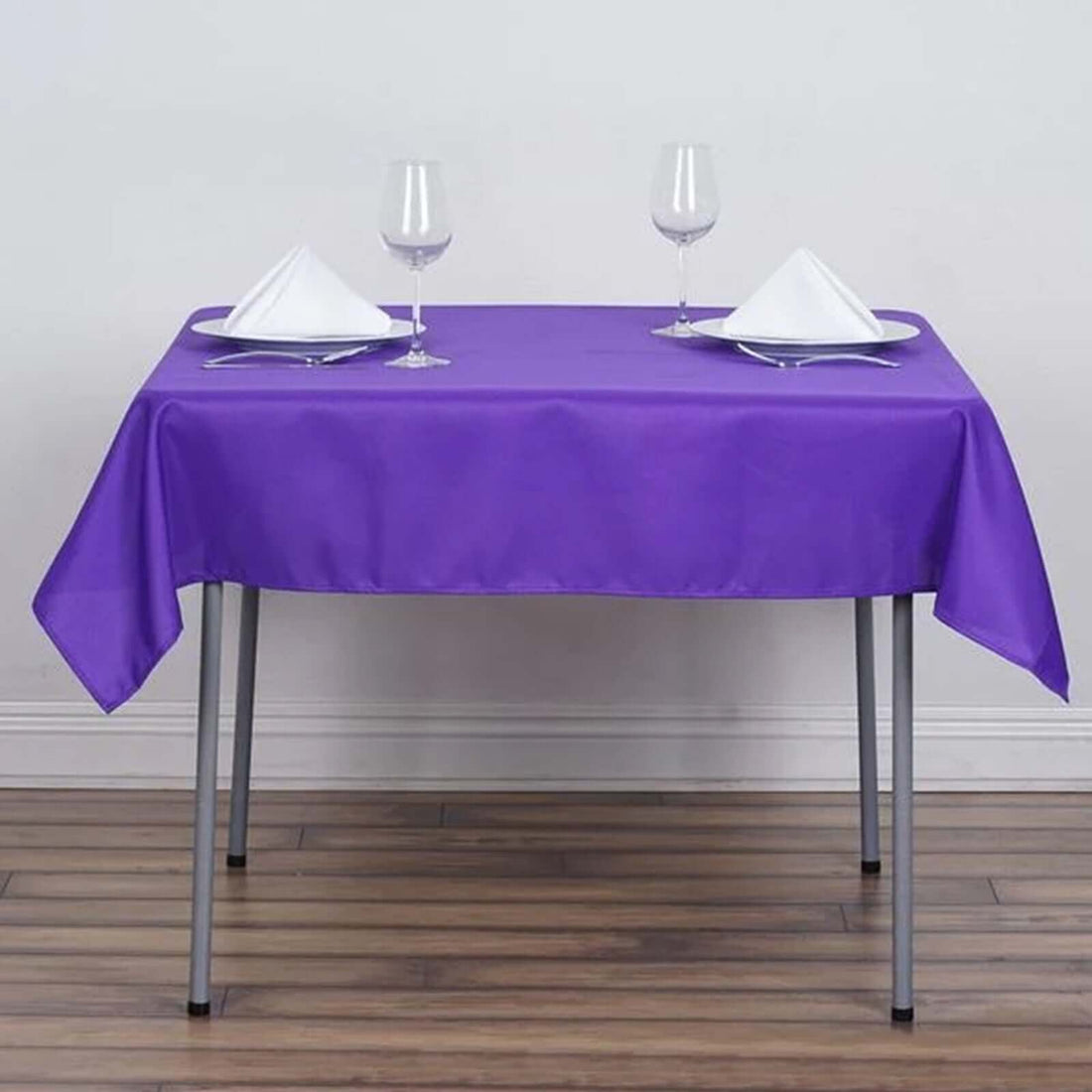 Purple tablecloth on a dining table set for two with glasses and napkins.