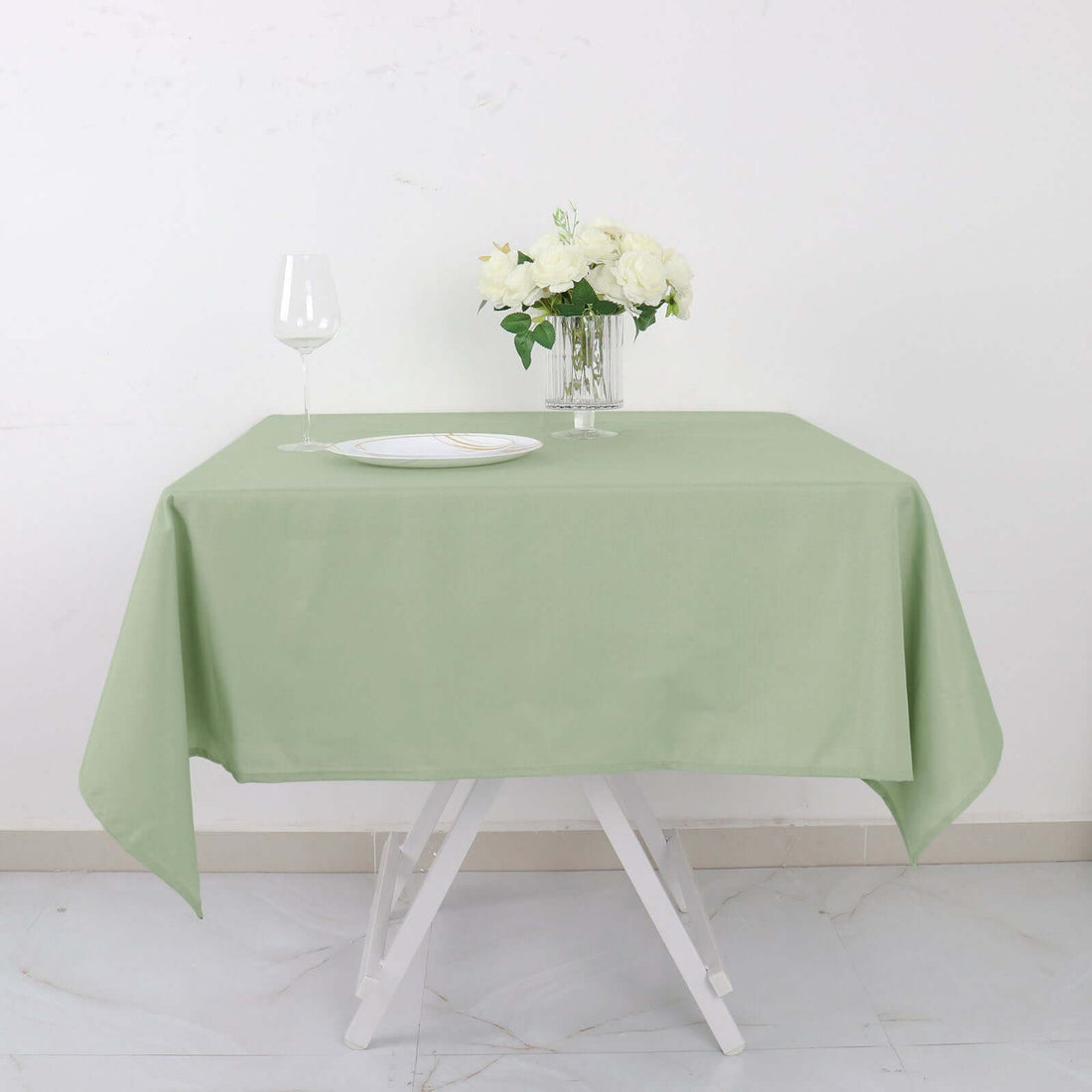 Green tablecloth draped on a white table with a glass and flowers.